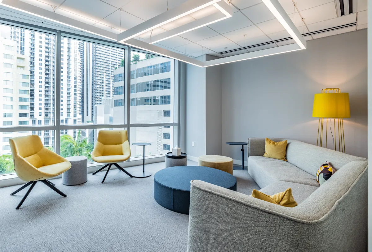 workspace featuring yellow swivel chairs, a gray sectional sofa, and floor-to-ceiling city views.